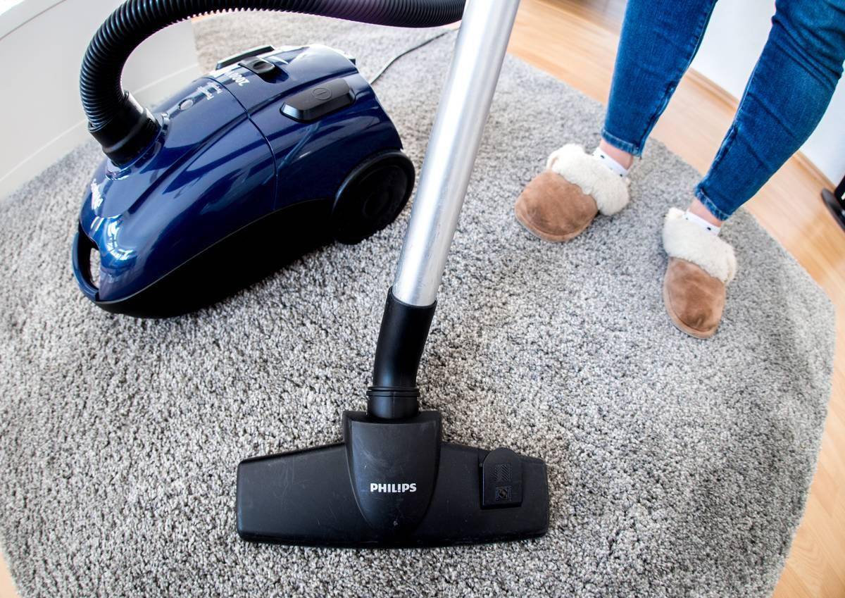 A woman vacuums her grey rug.