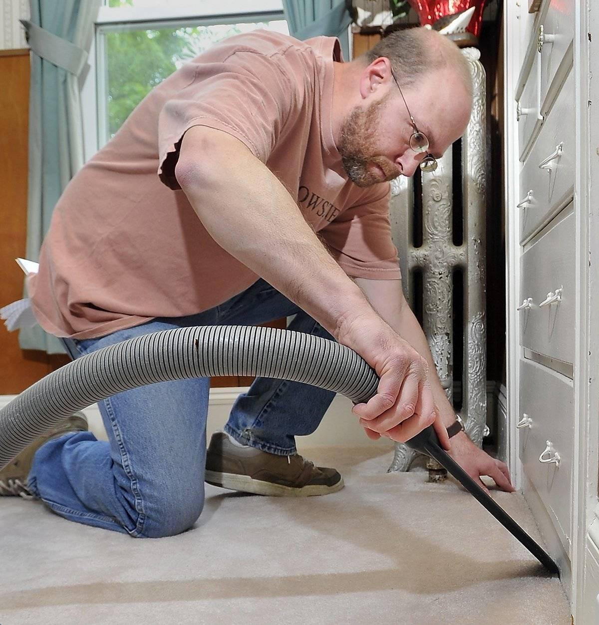 A man steam cleans a corner of a carpet.