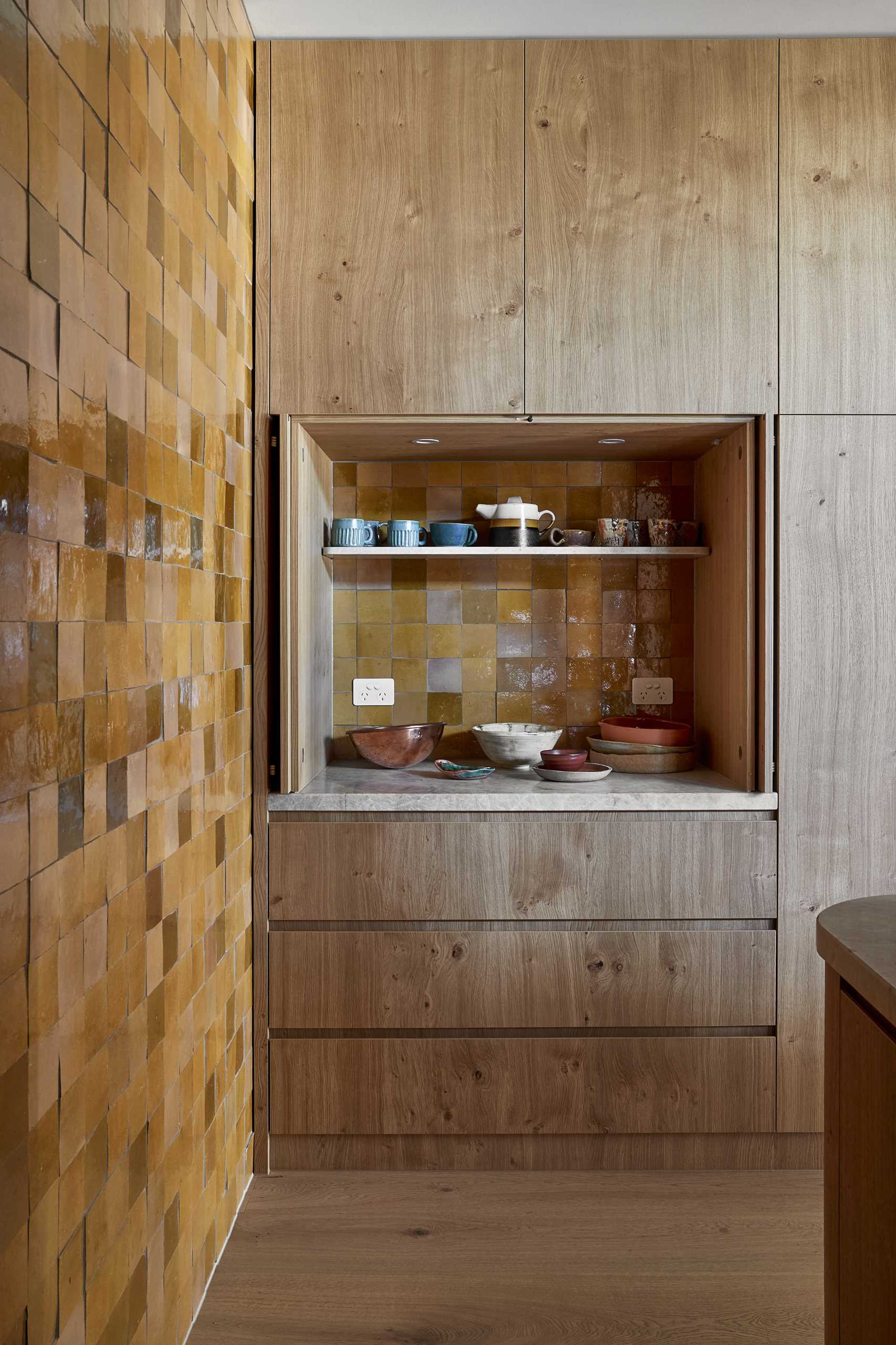 The kitchen is located at the end of the open-plan interior, with a tiled wall creating an eye-catching accent wall. Hidden from view is a pantry with additional storage and floating shelves.