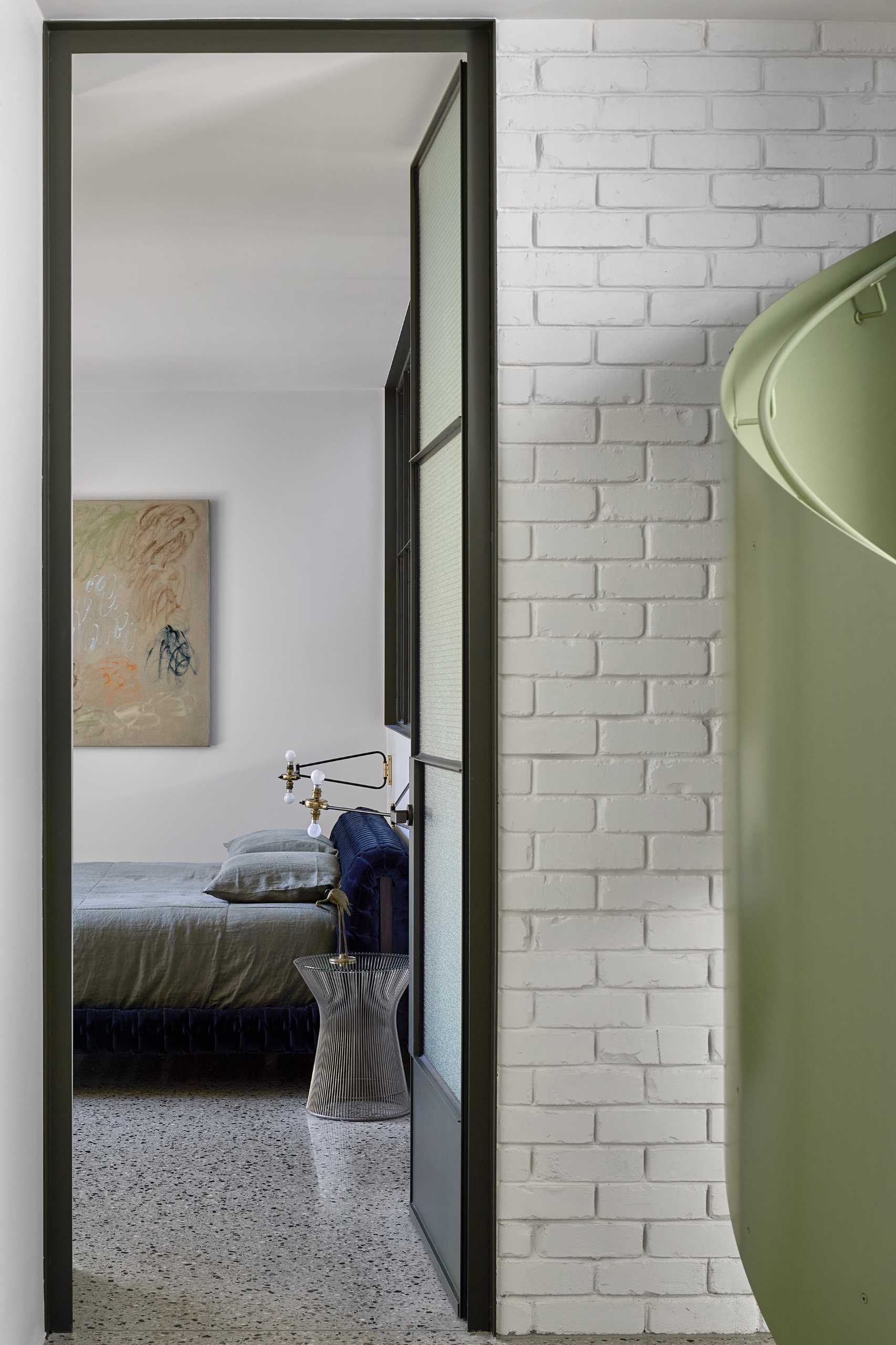 This modern main bedroom suite features a private landscaped courtyard, while a full-width steel window separates the bedroom from the green-drenched walls of handmade Spanish tiles and hanging plants in the en-suite bathroom.