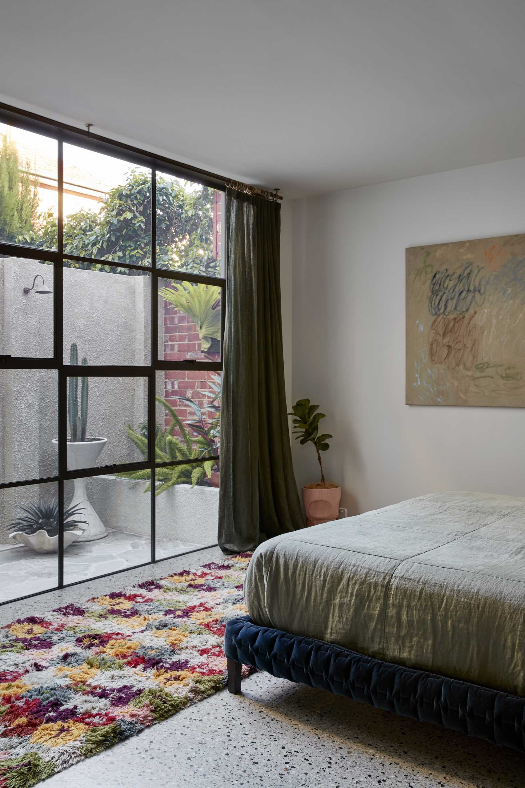 This modern main bedroom suite features a private landscaped courtyard, while a full-width steel window separates the bedroom from the green-drenched walls of handmade Spanish tiles and hanging plants in the en-suite bathroom.