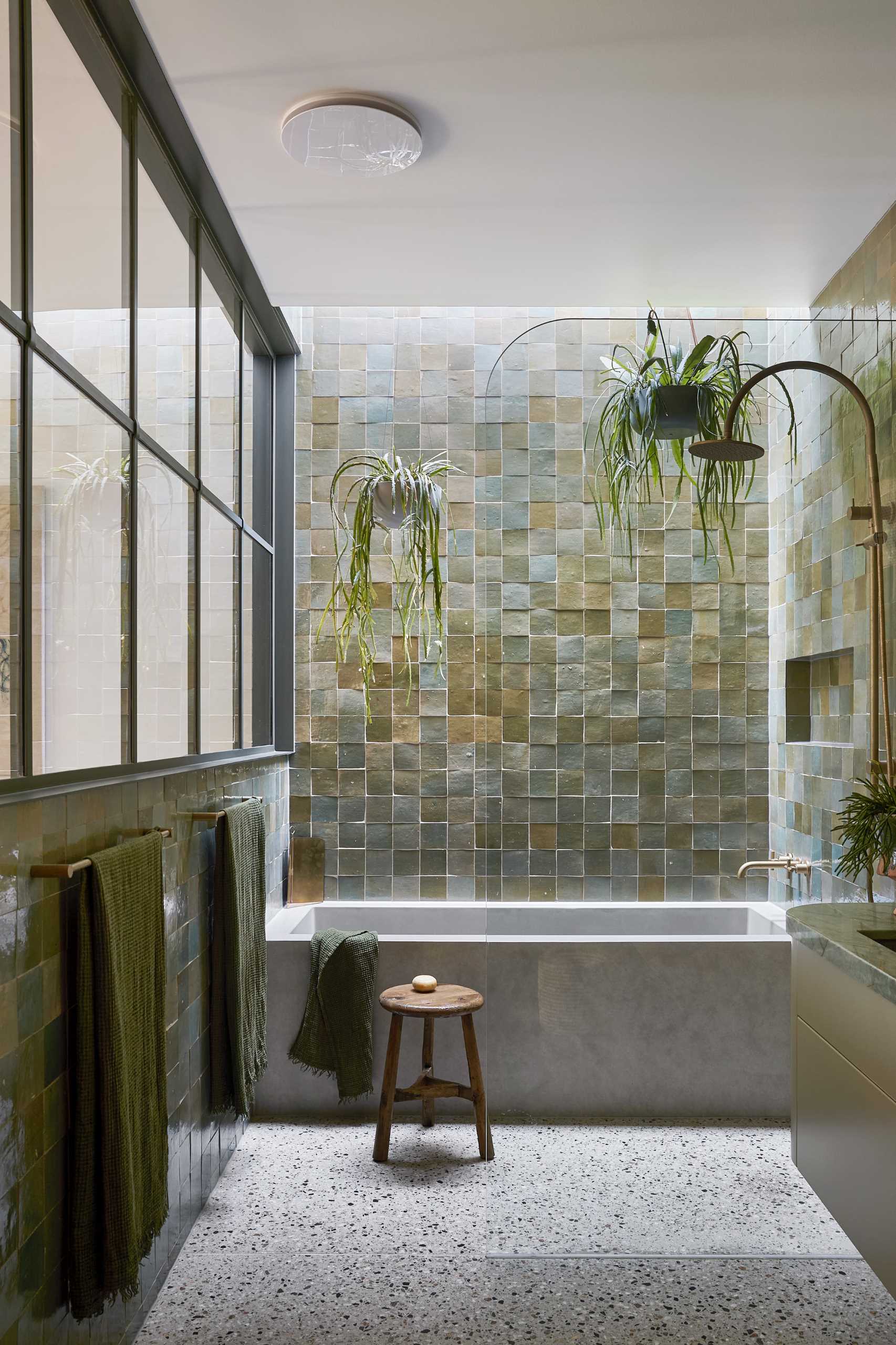 This modern main bedroom suite features a private landscaped courtyard, while a full-width steel window separates the bedroom from the green-drenched walls of handmade Spanish tiles and hanging plants in the en-suite bathroom.