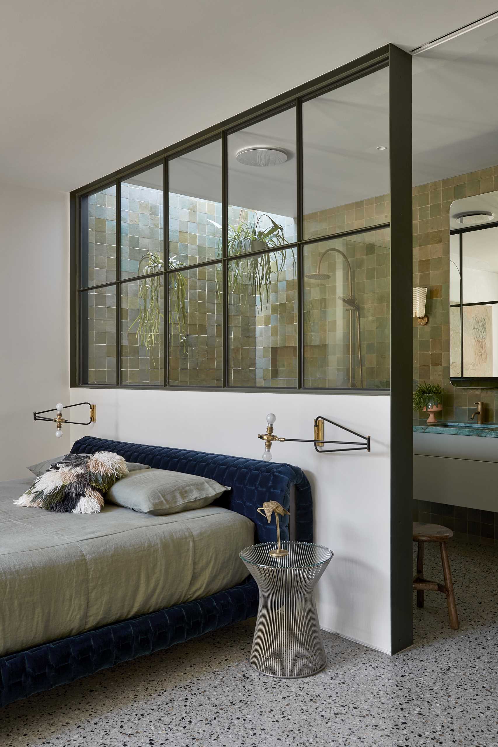 This modern main bedroom suite features a private landscaped courtyard, while a full-width steel window separates the bedroom from the green-drenched walls of handmade Spanish tiles and hanging plants in the en-suite bathroom.