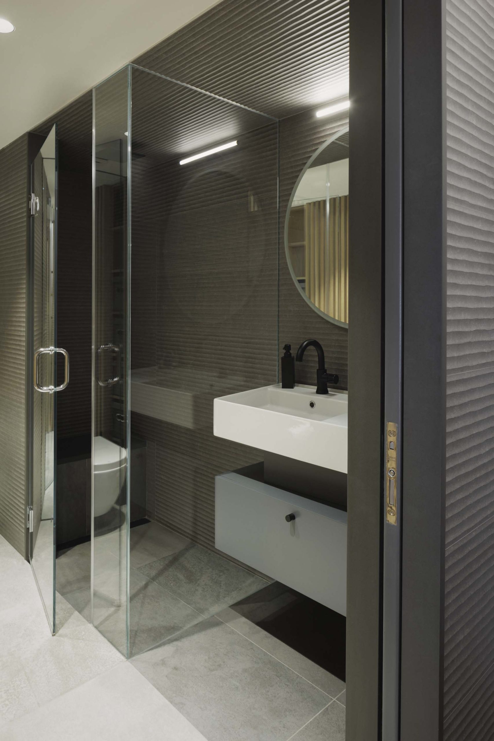 The slat wall continues in the bathroom, where it's been paired with striated slate gray and glass.