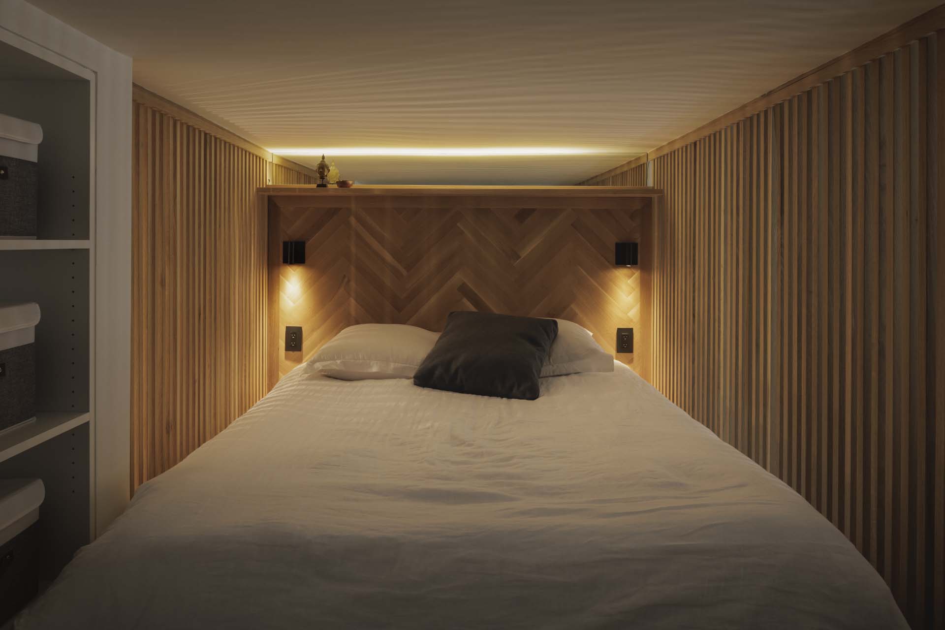 The lofted bedroom is lined with slat walls, while the headboard reflects the flooring pattern found throughout the apartment.