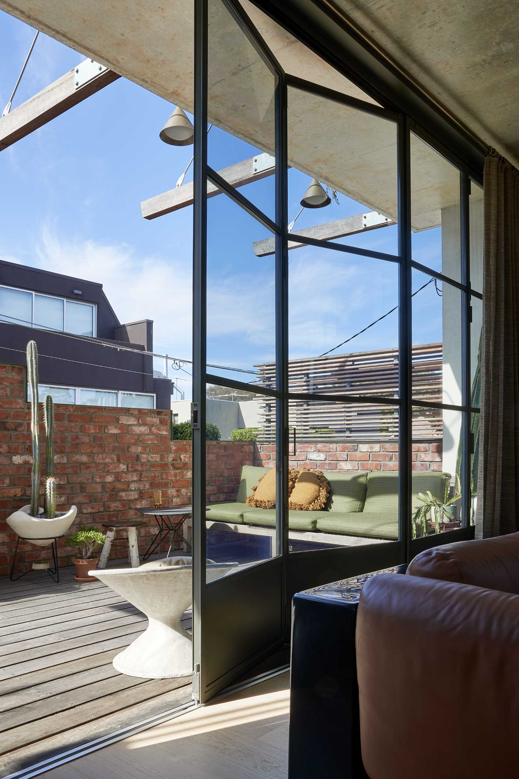 A folding steel and glass wall connects with the street-facing terrace tucked behind the stepped brick facade.